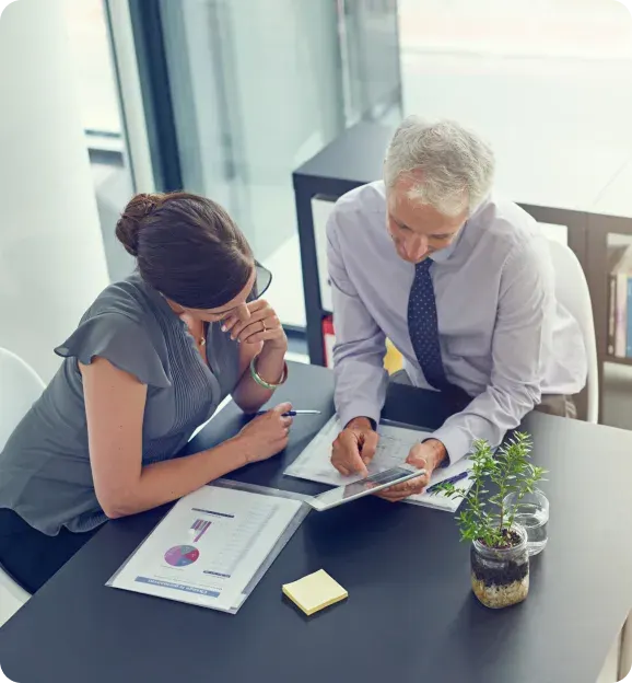 Two business professionals reviewing charts and data on papers and a tablet in a modern office.