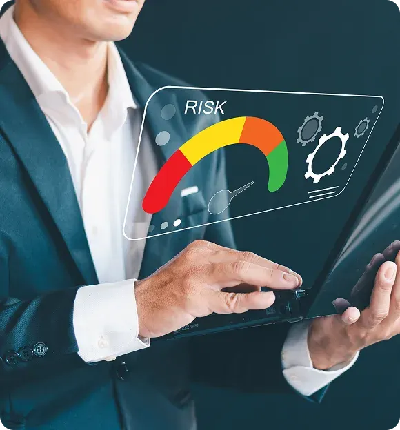 Businessman in suit holding a laptop with a digital risk meter gauge hovering above, indicating risk levels from red to green.
