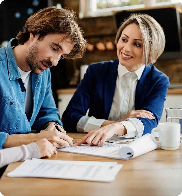 A man signing a document while a woman in business attire points at the paper and smiles.