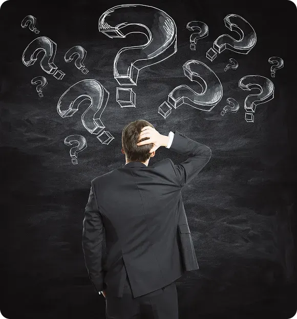 Man in suit scratching his head while looking at multiple large chalk-drawn question marks on a blackboard.