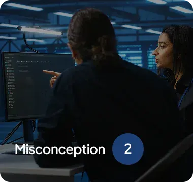 Two people discussing code displayed on a computer screen in a dimly lit office with the text 'Misconception 2' overlayed.