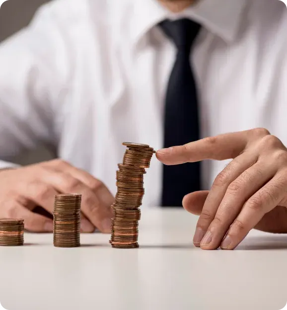 Person in a white shirt and black tie stacking pennies into uneven piles on a white table.