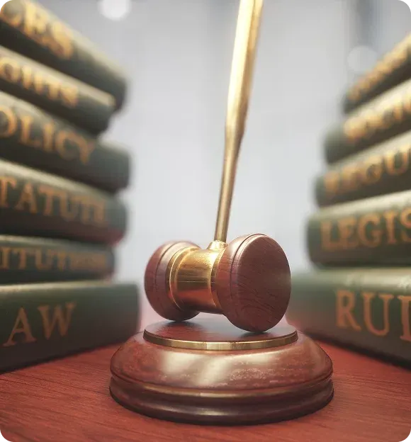 Wooden gavel with brass accents resting on a wooden surface, flanked by stacks of law books with gold lettering.