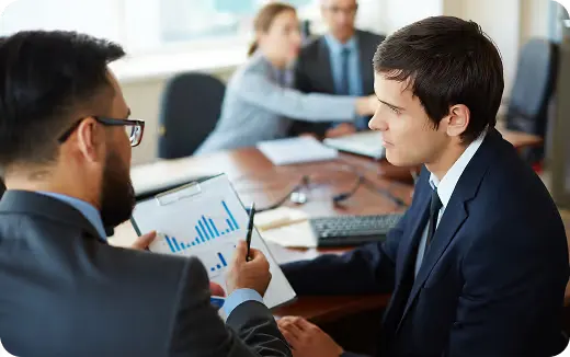 Business professionals discussing a chart with bar graphs around a conference table.