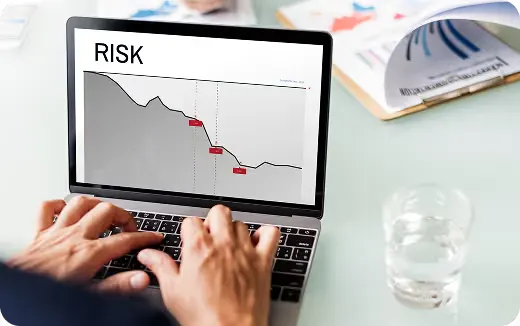 Person analyzing a declining risk graph on a laptop with documents and a glass of water on the desk.