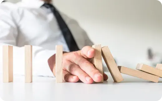 A person in a white shirt and black tie stops falling wooden dominoes with their hand on a table.