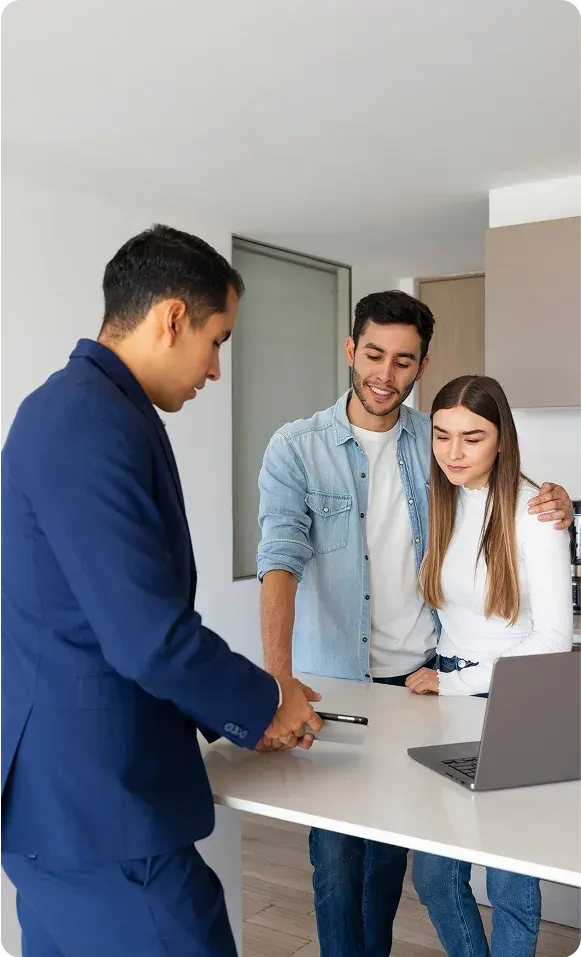 Real estate agent showing a phone to a couple standing together at a kitchen counter with a laptop nearby.